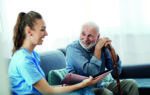 Doctor or nurse caregiver showing a brochure to senior man at home or nursing home