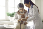 Mature lady sitting on exam bed learning to download health tracker for senior citizens